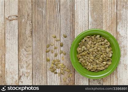 pumpkin seeds in a green ceramic bowl on grunge white painted wood table