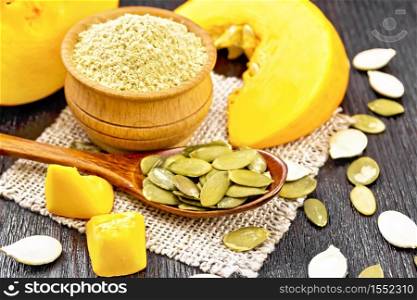 Pumpkin seeds in a spoon on a burlap, flour in a bowl, slices of vegetable on dark wooden board background