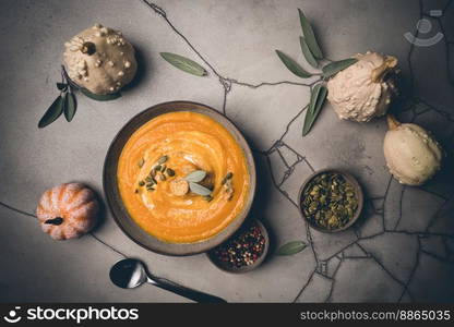 Pumpkin soup and organic pumpkins, top view, gray background. Seasonal autumn food - Spicy pumpkin soup with cream and pumpkin seeds.. Spicy pumpkin soup