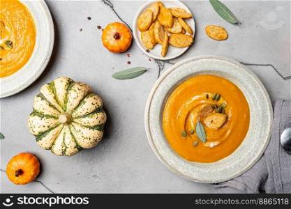 Pumpkin soup and organic pumpkins, top view, gray background. Seasonal autumn food - Spicy pumpkin soup with cream, croutons and pumpkin seeds.. Spicy pumpkin soup
