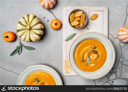 Pumpkin soup and organic pumpkins, top view, gray background. Seasonal autumn food - Spicy pumpkin soup with cream, croutons and pumpkin seeds.. Spicy pumpkin soup