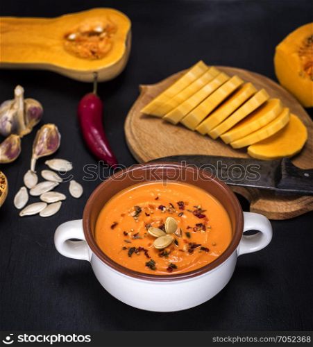 pumpkin soup in a ceramic plate and pieces of pumpkin on a black background, top view