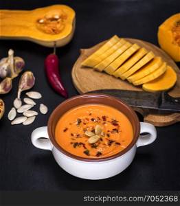 pumpkin soup in a ceramic plate and pieces of pumpkin on a black background, top view