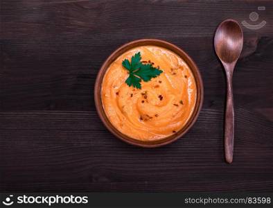 pumpkin soup in a round clay plate and a wooden spoon, top view