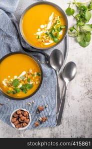 Pumpkin soup in bowl garnished with cream, hazelnut and watercress. Top view. Comfort food. Cream of pumpkin squash soup