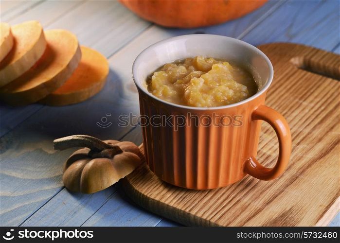 pumpkin soup in the orange bowl on blue wooden background