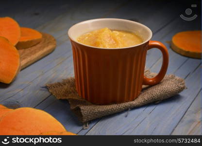 pumpkin soup in the orange bowl on blue wooden background