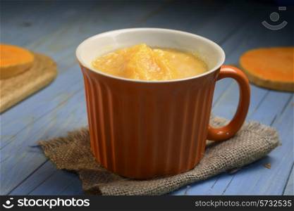 pumpkin soup in the orange bowl on blue wooden background