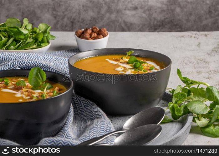 Pumpkin soup with watercress on table. Seasonal autumn food - Spicy pumpkin soup in bowl.