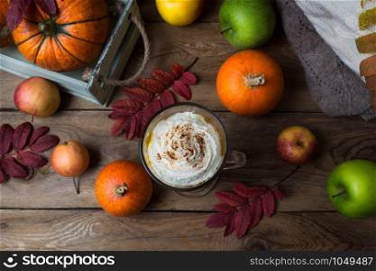 Pumpkin spice coffee latte mug with whipped cream and cocoa, fall leaves, pumpkin, knitted plaid and apples, top view