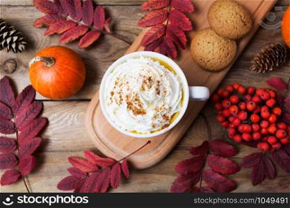 Pumpkin spice coffee latte mug with whipped cream, cookies, fall leaves and rowan berries, top view