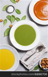Pumpkin, tomato and spinach soups over grey concrete background, top view. Clean eating, dieting, vegan, vegetarian, healthy food concept