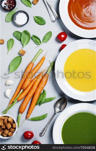 Pumpkin, tomato and spinach soups over grey concrete background, top view. Clean eating, dieting, vegan, vegetarian, healthy food concept