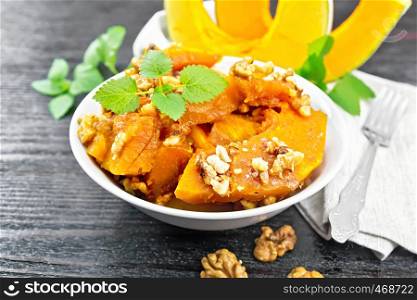 Pumpkin with walnuts and honey in a bowl, napkin and mint on a black wooden board background