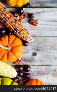 Pumpkins,corn,apples,nuts and cranberries on wooden background