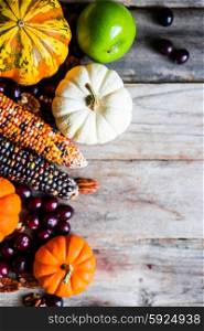 Pumpkins,corn,apples,nuts and cranberries on wooden background