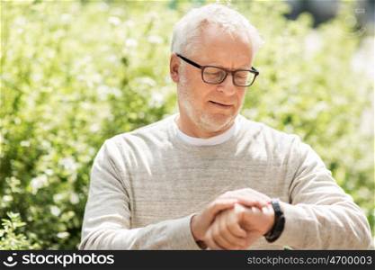 punctuality and people concept - senior man checking time on his wristwatch or smartwatch in city. senior man checking time on his wristwatch