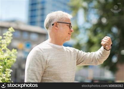 punctuality and people concept - senior man checking time on wristwatch or smart watch on his hand in city. senior man checking time on his wristwatch