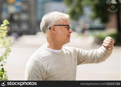 punctuality and people concept - senior man checking time on wristwatch or smart watch on his hand in city. senior man checking time on his wristwatch