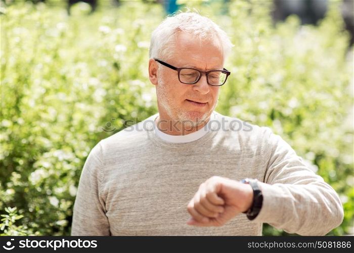 punctuality and people concept - senior man checking time on wristwatch or smart watch on his hand outdoors. senior man checking time on his wristwatch