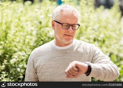 punctuality and people concept - senior man checking time on wristwatch or smart watch on his hand outdoors. senior man checking time on his wristwatch