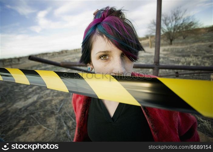 Punk girl outdoors behind a strip of yellow and black caution tape