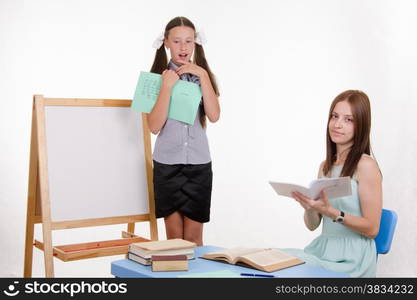 Pupil stands at the blackboard, the teacher sits at his desk and listens to the student