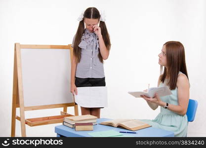 Pupil stands at the blackboard, the teacher sits at his desk and listens to the student