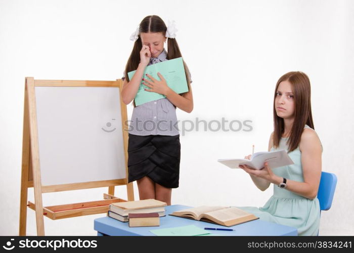 Pupil stands at the blackboard, the teacher sits at his desk and listens to the student