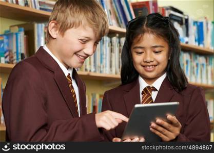 Pupils Wearing School Uniform Using Digital Tablet In Library