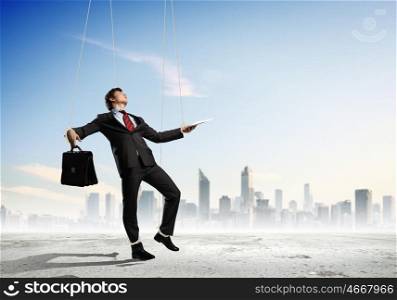 Puppet businessman. Image of businessman hanging on strings like marionette against city background. Conceptual photography