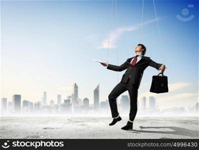 Puppet businessman. Image of businessman hanging on strings like marionette against city background. Conceptual photography