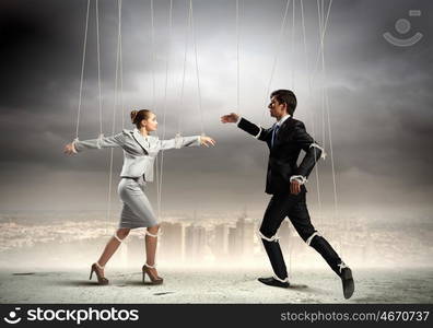 Puppet businesspeople. Image of businesspeople hanging on strings like marionettes against city background. Conceptual photography