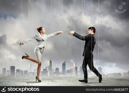 Puppet businesspeople. Image of businesspeople hanging on strings like marionettes against city background. Conceptual photography
