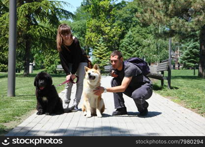 Puppies of Akita Inu and Newfaundlander posing with their owners in public park
