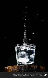 Pure fresh water in glass, an effervescent tablet with vitamin C falls into the glass, splashing over the water, dark background with copy space for text, selective focus. Close-up, vertical frame