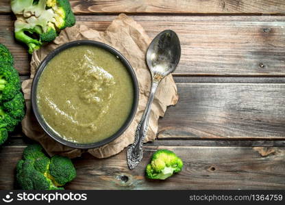 Puree broccoli in a bowl with a spoon. On a wooden background.. Puree broccoli in a bowl with a spoon.