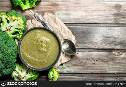Puree broccoli in a bowl with a spoon. On a wooden background.. Puree broccoli in a bowl with a spoon.