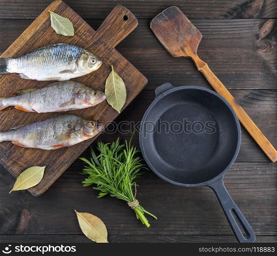 Purified river fish from the scales on brown wooden board, beside an empty round black cast-iron pan, top view. Purified river fish from the scales