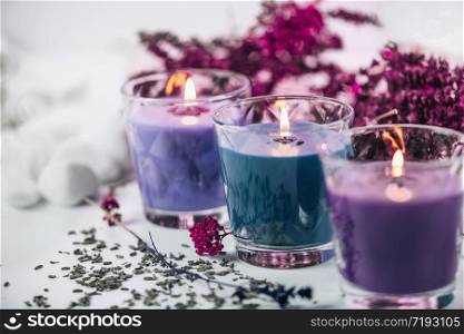 Purple and blue scented candles with lavender and dried flowers decoration on a white table.. Aromatic Purple and Blue Scented Candles with Lavender Decoration