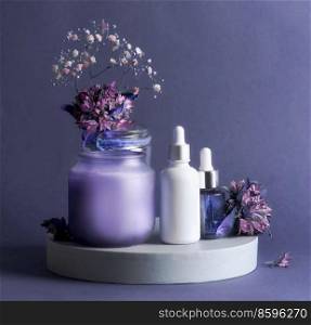 Purple beauty product setting with cosmetic serum bottles, candle and flowers. Healthy skin care products for facial treatment. Front view with copy space.