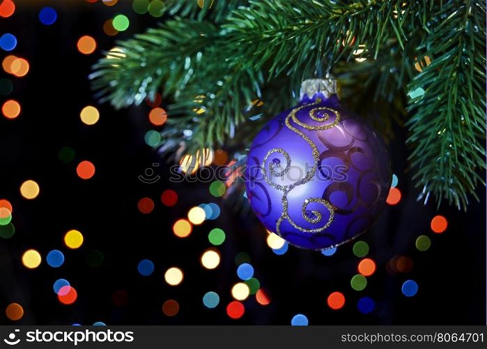 purple Christmas ball hanging on a Christmas tree branch on a black background with colored bokeh