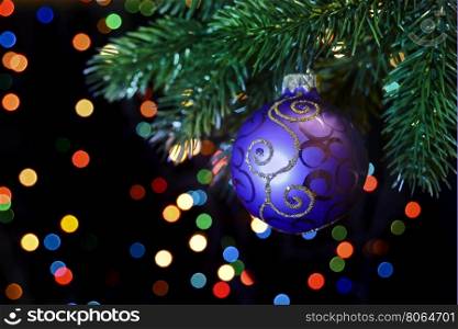 purple Christmas ball hanging on a Christmas tree branch on a black background with colored bokeh