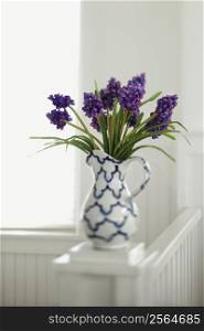 Purple flowers arranged in pitcher vase.
