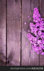Purple lilac branch on brown wooden surface, empty space in the middle