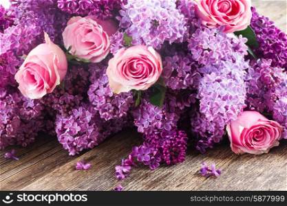 Purple Lilac flowers with pink roses on wooden table . Lilac flowers