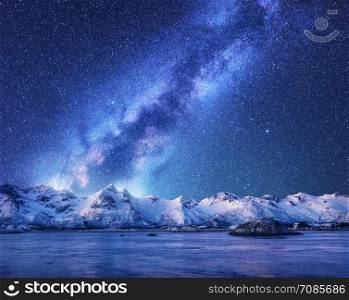 Purple Milky Way over snow covered mountains and sea at night in winter in Norway. Landscape with snowy rocks, sky with stars, reflection in water, fjord. Lofoten Islands. Space. Beautiful milky way