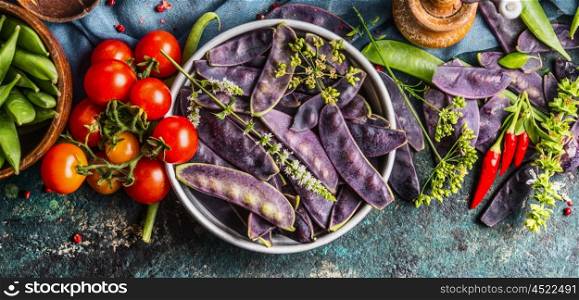 Purple pea pods in metal bowl with tomatoes and cooking ingredients, top view. Healthy vegetarian food concept