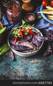 Purple pea pods with cooking ingredients in bows on rustic kitchen table, top view