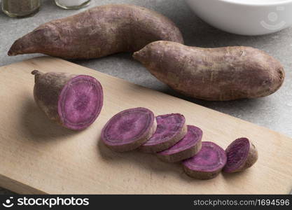 Purple sweet potatoes and a sliced one on a cutting board close up